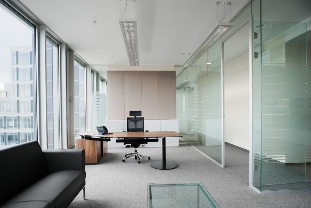 An office has a set of windows and a wall made out of soundproof glass.
