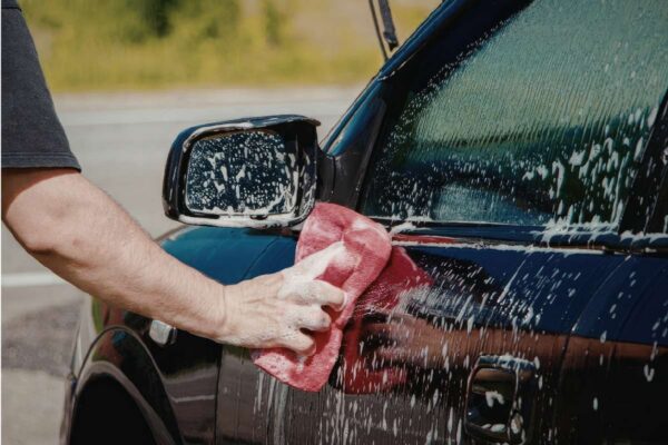 The owner of a vehicle uses an abrasive rag while polishing his cars windows.